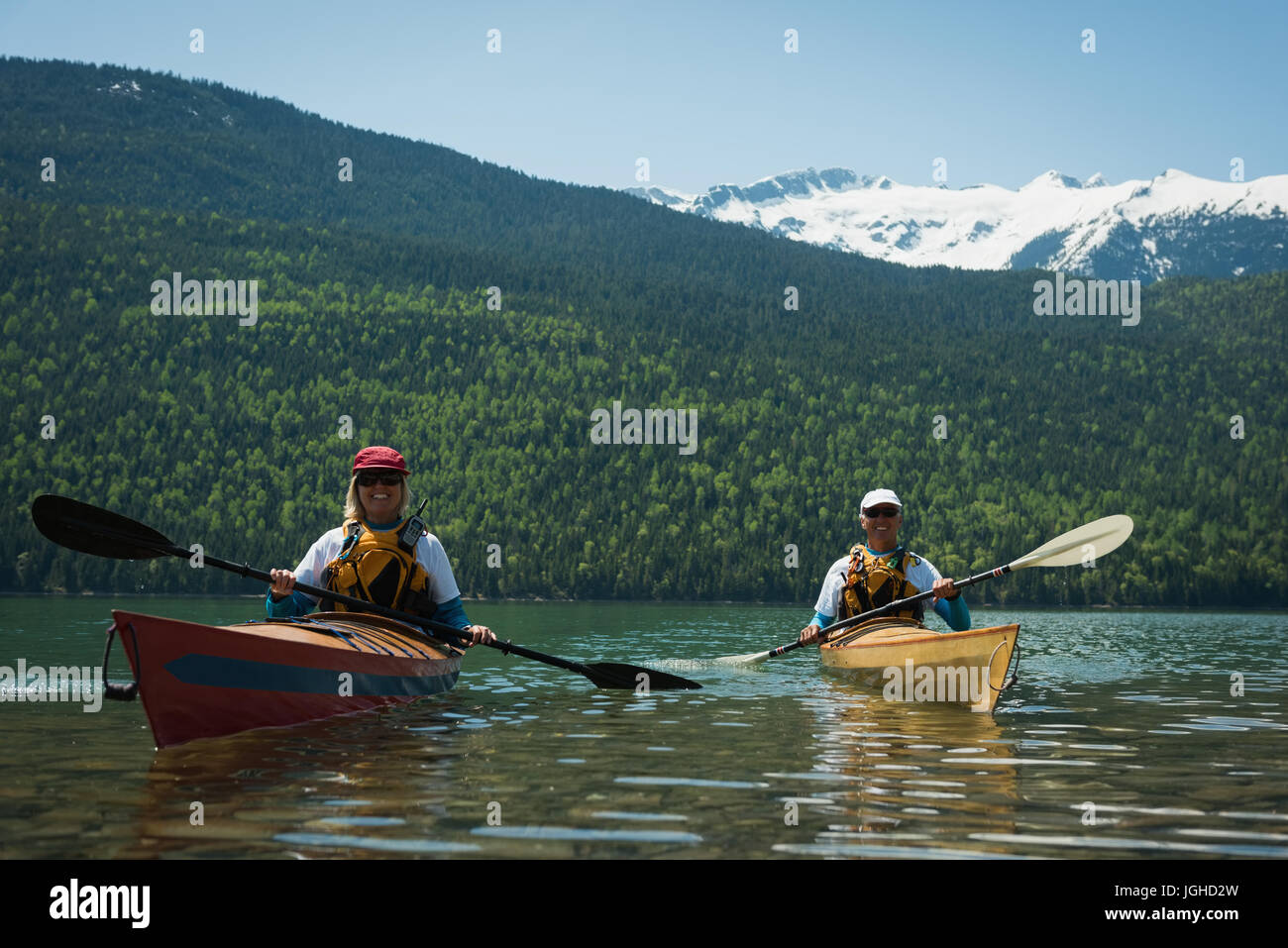 Couple portant des gilets tout en kayak dans le lac contre snowcapped mountain Banque D'Images