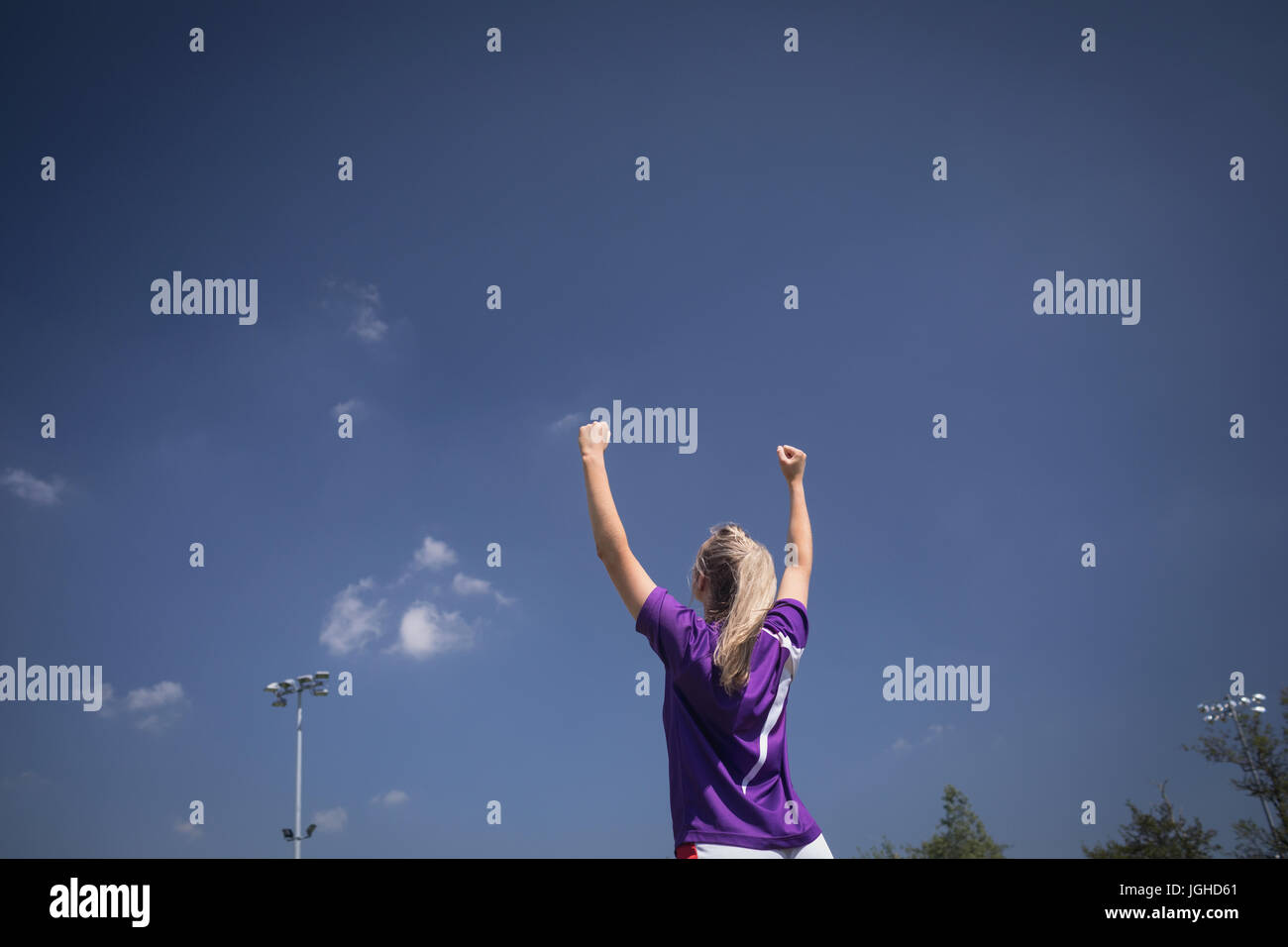 Vue arrière du joueur de soccer féminin avec bras levés contre le ciel bleu Banque D'Images