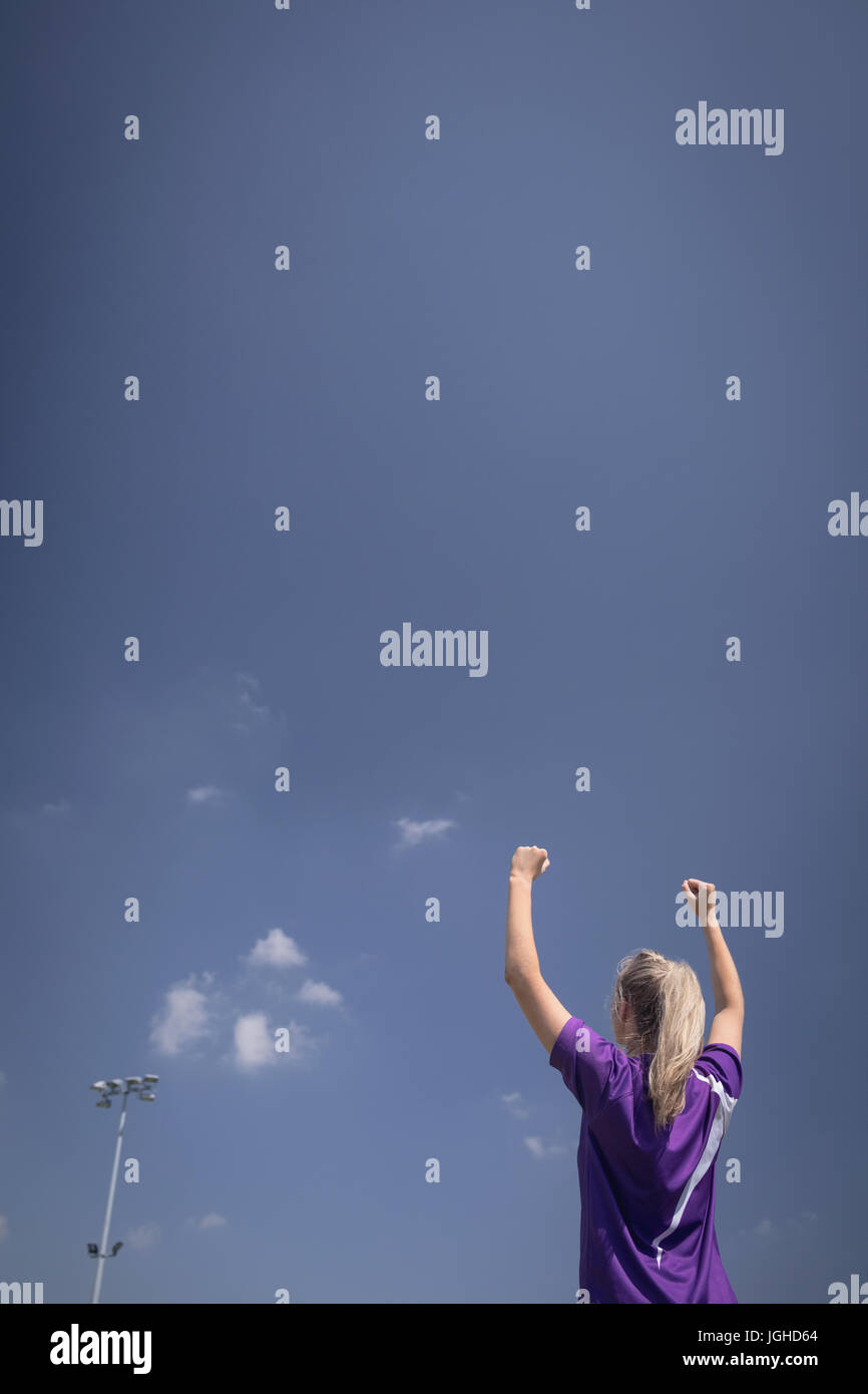 Vue arrière du joueur de soccer féminin avec bras levés contre le ciel bleu Banque D'Images