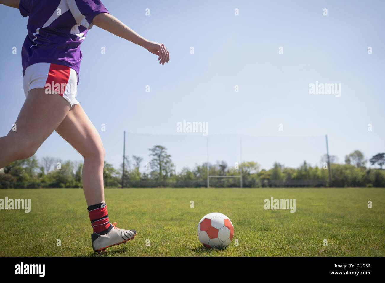 La section basse de femme jouant au football sur terrain contre ciel clair Banque D'Images