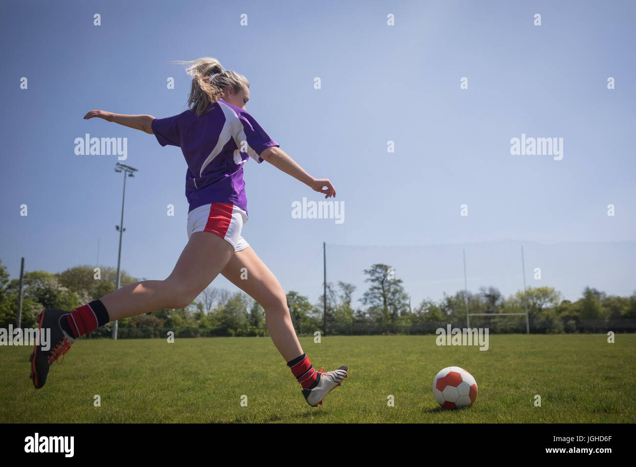 Toute la longueur de jeune femme jouant au football sur terrain contre ciel clair Banque D'Images