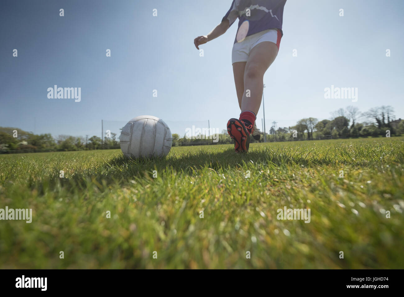 La section basse de femme jouant au football sur terrain contre ciel lors de journée ensoleillée Banque D'Images