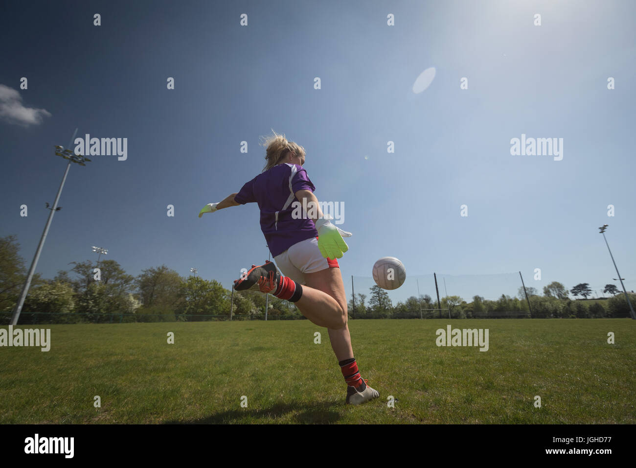 Vue arrière pleine longueur du female player jouant au football sur terrain against sky Banque D'Images