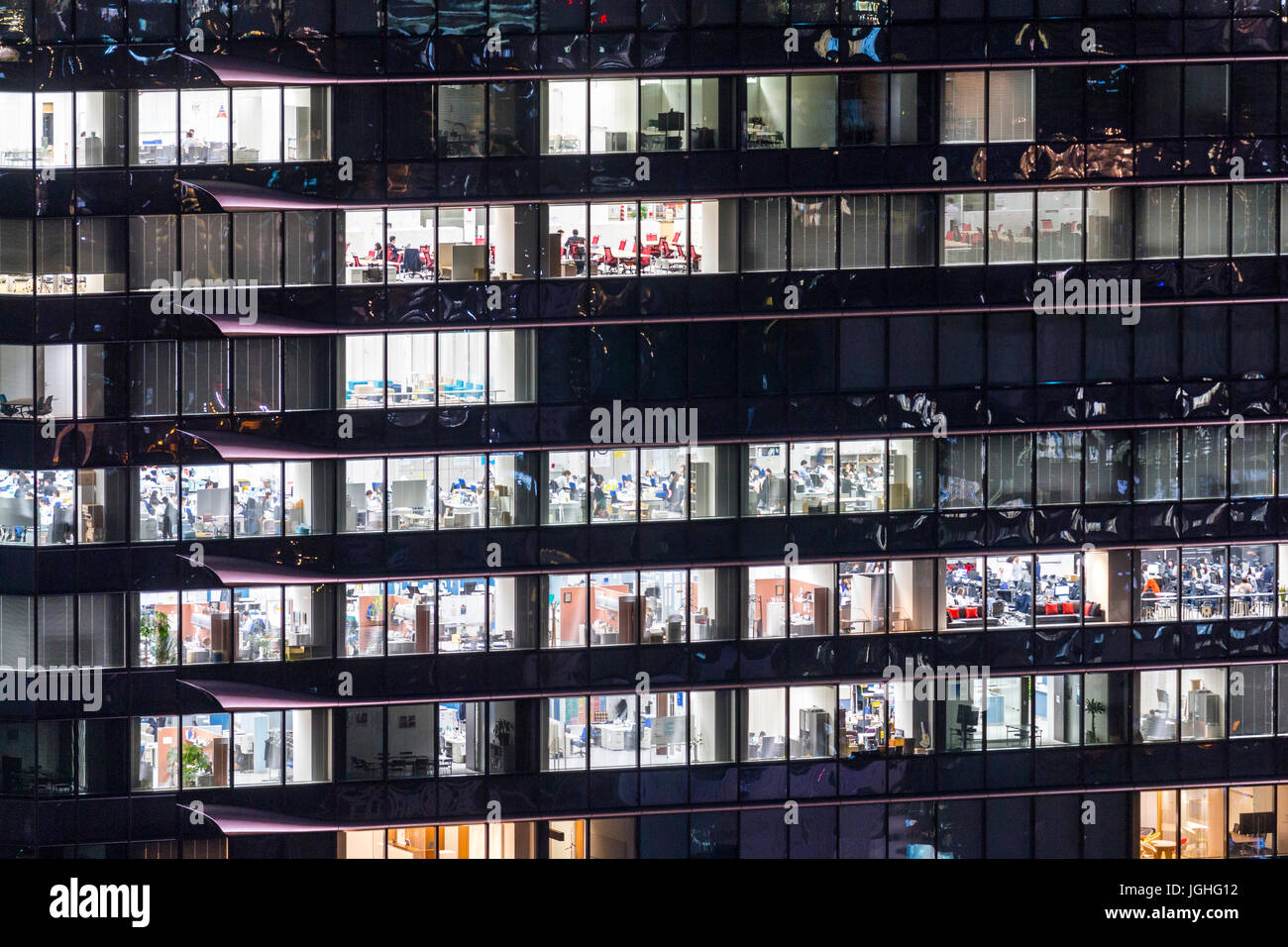 Immeuble de bureaux, Close up de windows sur le côté de la nuit noire, avec différents bureaux et les fenêtres éclairées avec les travailleurs à l'intérieur d'Osaka, au Japon. Banque D'Images