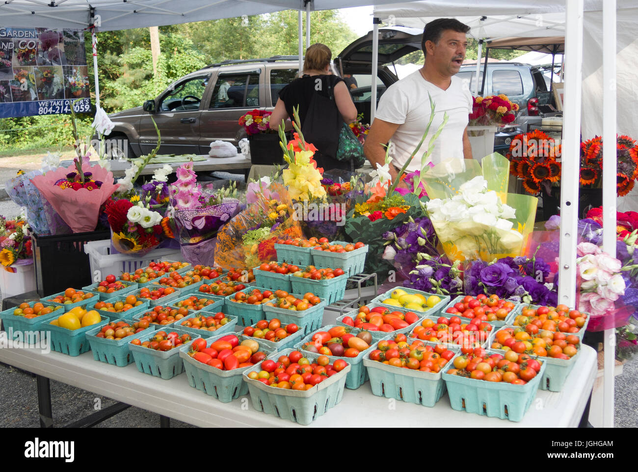 Vendeur de produits frais du marché avec des tomates et des fleurs fraîches Banque D'Images