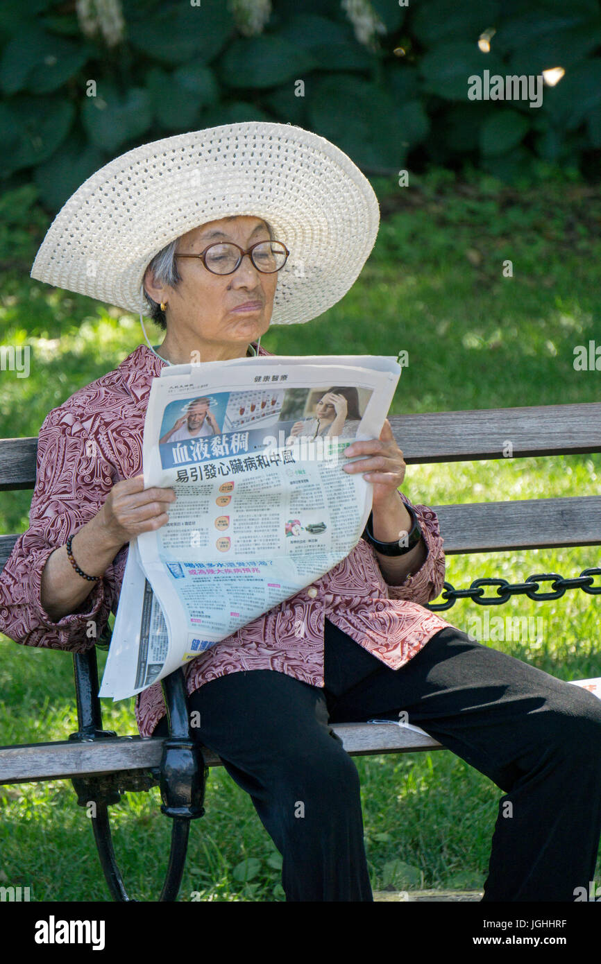 Une cuisine asiatique dans un floppy hat de lire le journal dans Washington Square Park à Manhattan, New York City. Banque D'Images