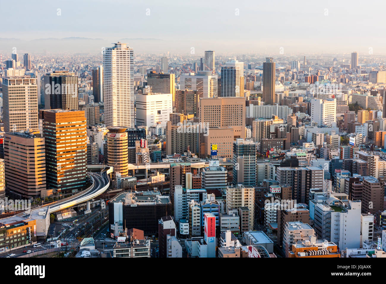 Vue du haut des gratte-ciel Umeda, à Osaka. Ville illuminée par la lumière au coucher du soleil, heure d'or. Hôtels et bureaux de grande hauteur, au-delà des montagnes brumeuses. Banque D'Images