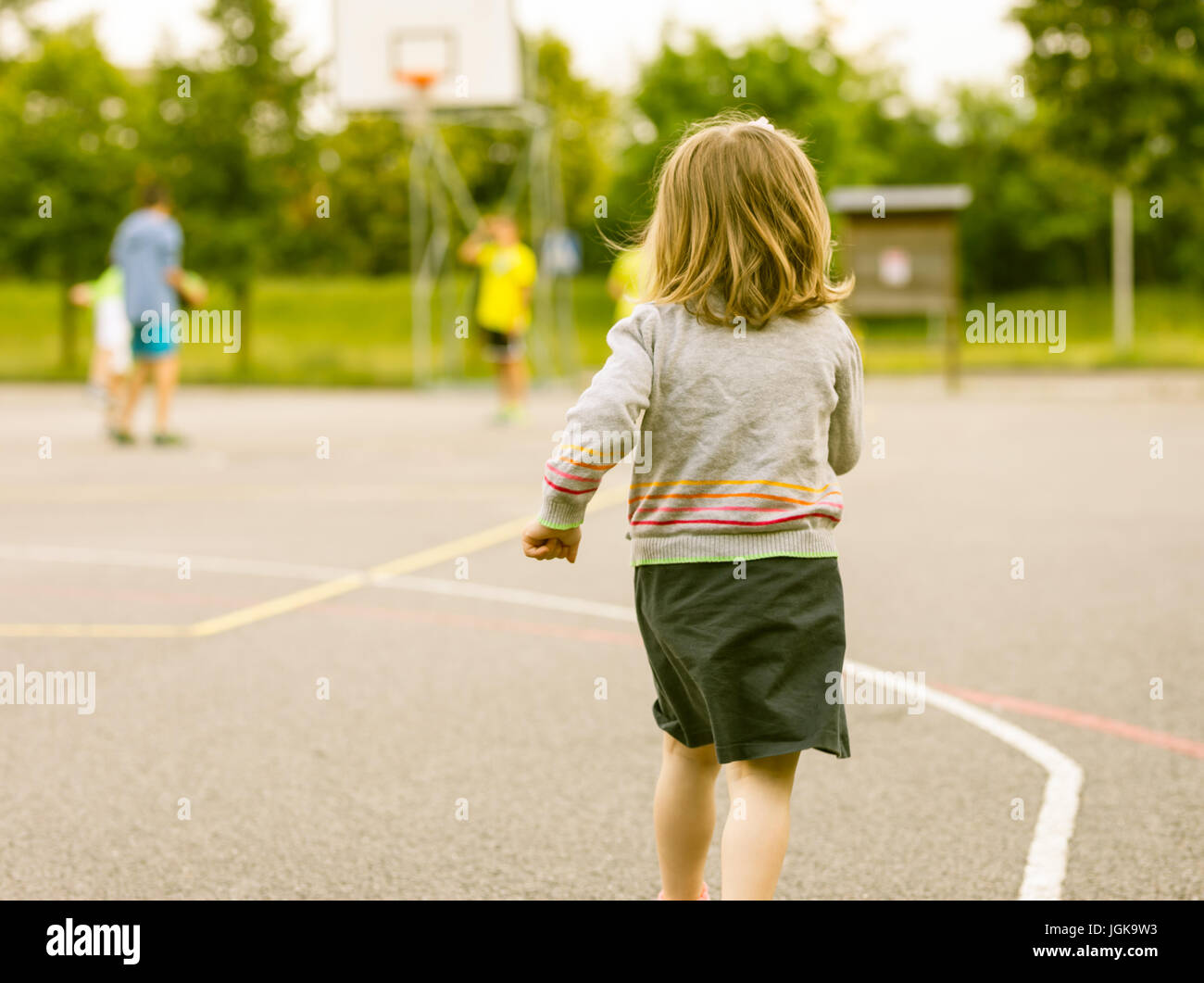 Petite fille courir vers plus grands garçons jouant des sports dans un  terrain de basket-ball Photo Stock - Alamy
