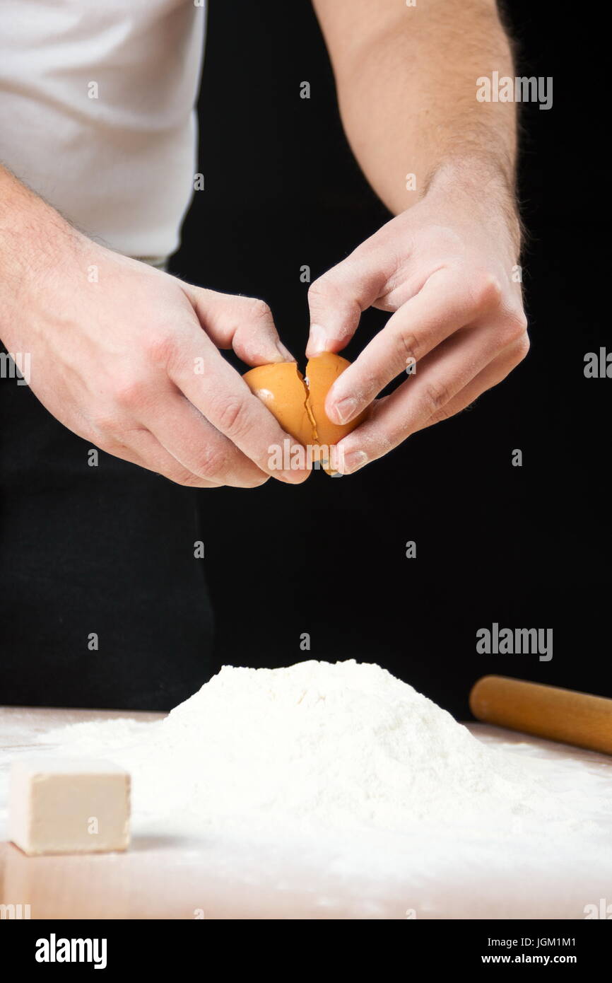 Male chef d'oeufs d'ouverture au-dessus de la farine dans le processus fabrication du pain Banque D'Images