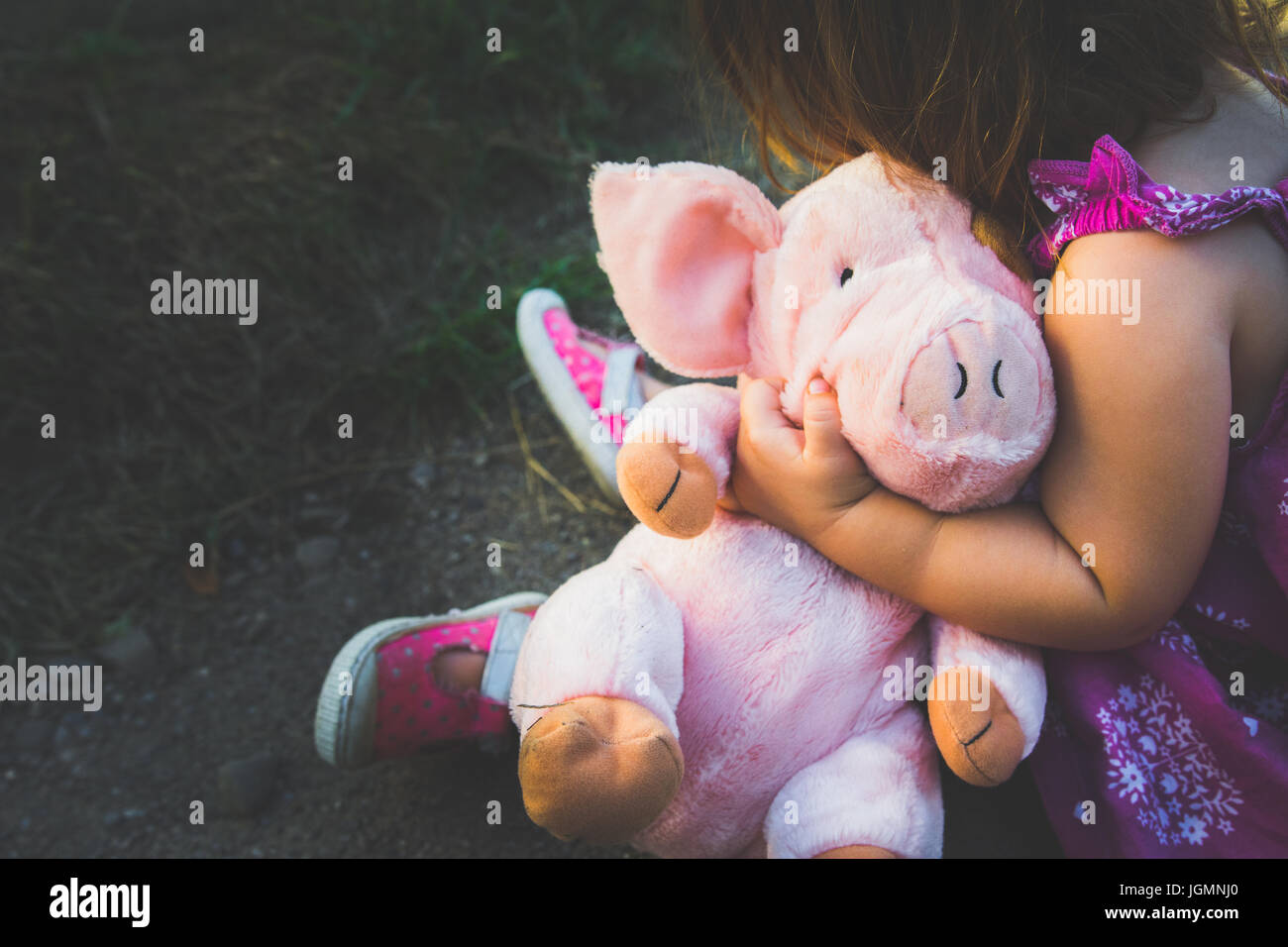 Un jeune enfant de sexe féminin est titulaire d'un cochon en peluche rose. Banque D'Images