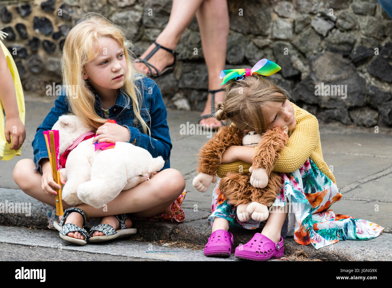 Deux jeunes enfants de race blanche, les filles, de 5 à 6 ans, assis sur le trottoir de la chaussée, regardant quelque chose (invisible) avec leurs ours et de l'orang-outan. Banque D'Images