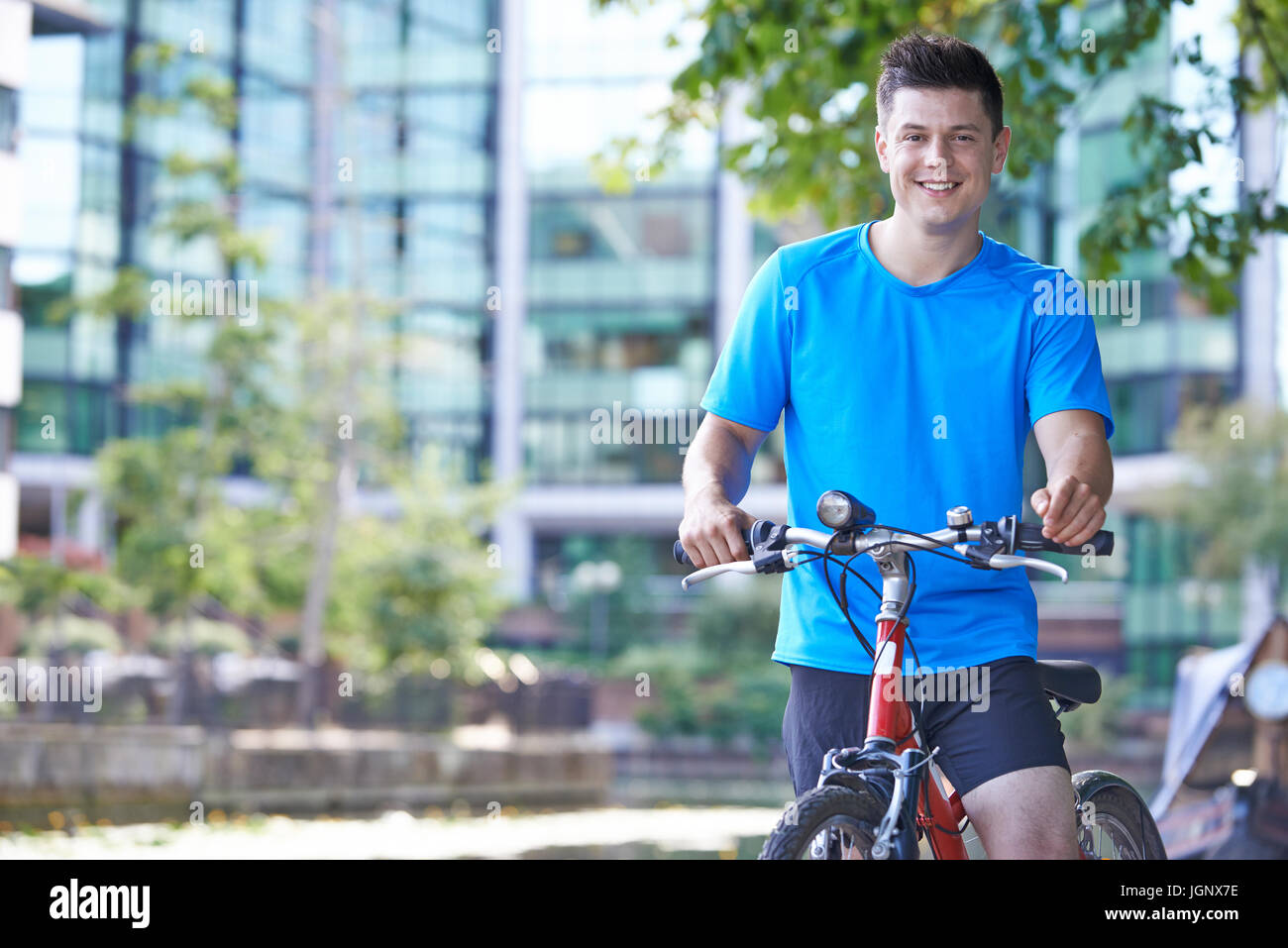 Portrait de jeune homme à vélo à côté de rivière en milieu urbain Banque D'Images