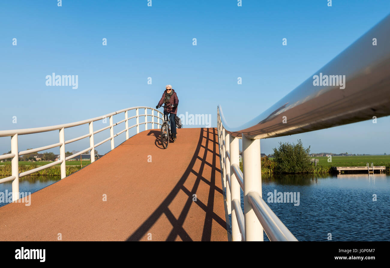 Groot-Ammers, Pays-Bas - le 11 novembre 2016 : l'architecture moderne d'un pont sur le vélo d'un petit canal avec trois coureurs à Groot-Ammers dans t Banque D'Images