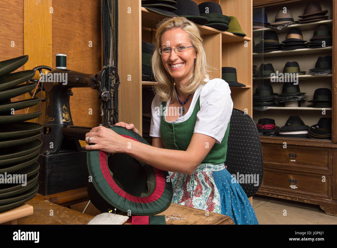 Woman ruban de soie couture et doublure intérieure sur hat edge, chapeaux finis sur des étagères derrière, modiste atelier, Bad Aussee, Styrie Banque D'Images