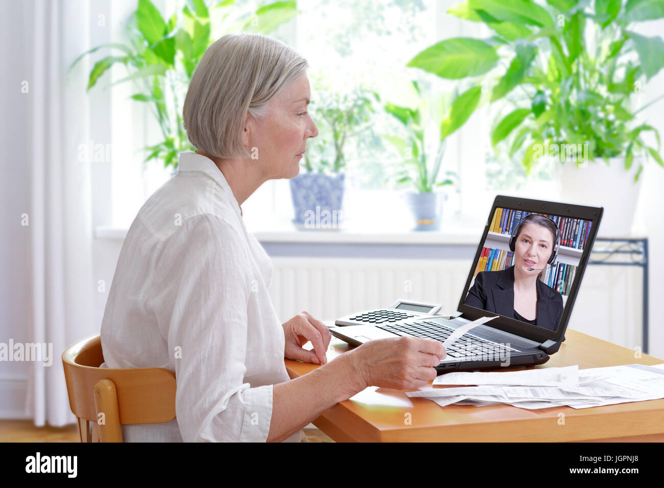 Femme senior à la maison avec son ordinateur portable et un bon nombre d'accusés de réception, l'écoute d'un comptable avant de faire sa déclaration fiscale annuelle, conseils fiscaux en ligne conc Banque D'Images