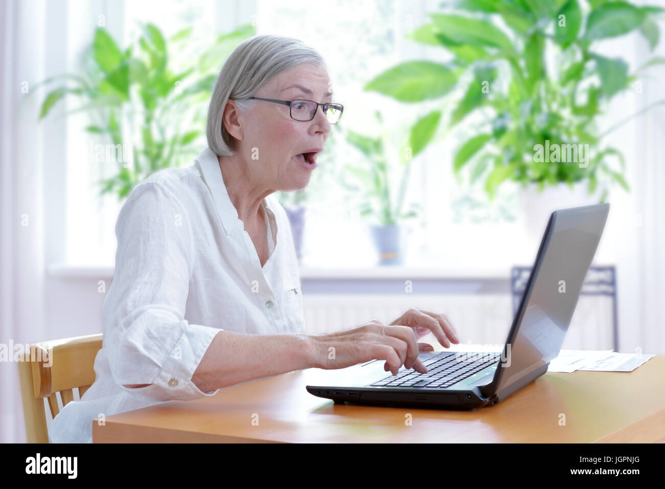 Femme senior à la maison dans son salon en regardant un choc à l'écran de son ordinateur portable, internet security concept Banque D'Images