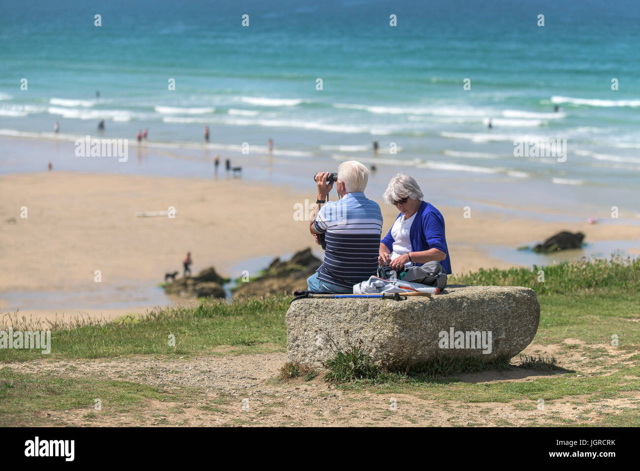 Les vacanciers âgés assis sur un rocher sur la plage donnant sur la plage de fistral, Newquay, Cornwall. Banque D'Images