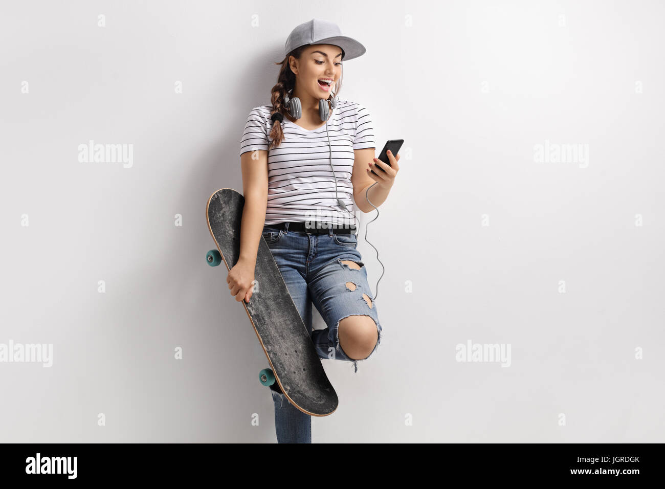 Adolescente avec un téléphone et skateboard appuyé contre un mur Banque D'Images