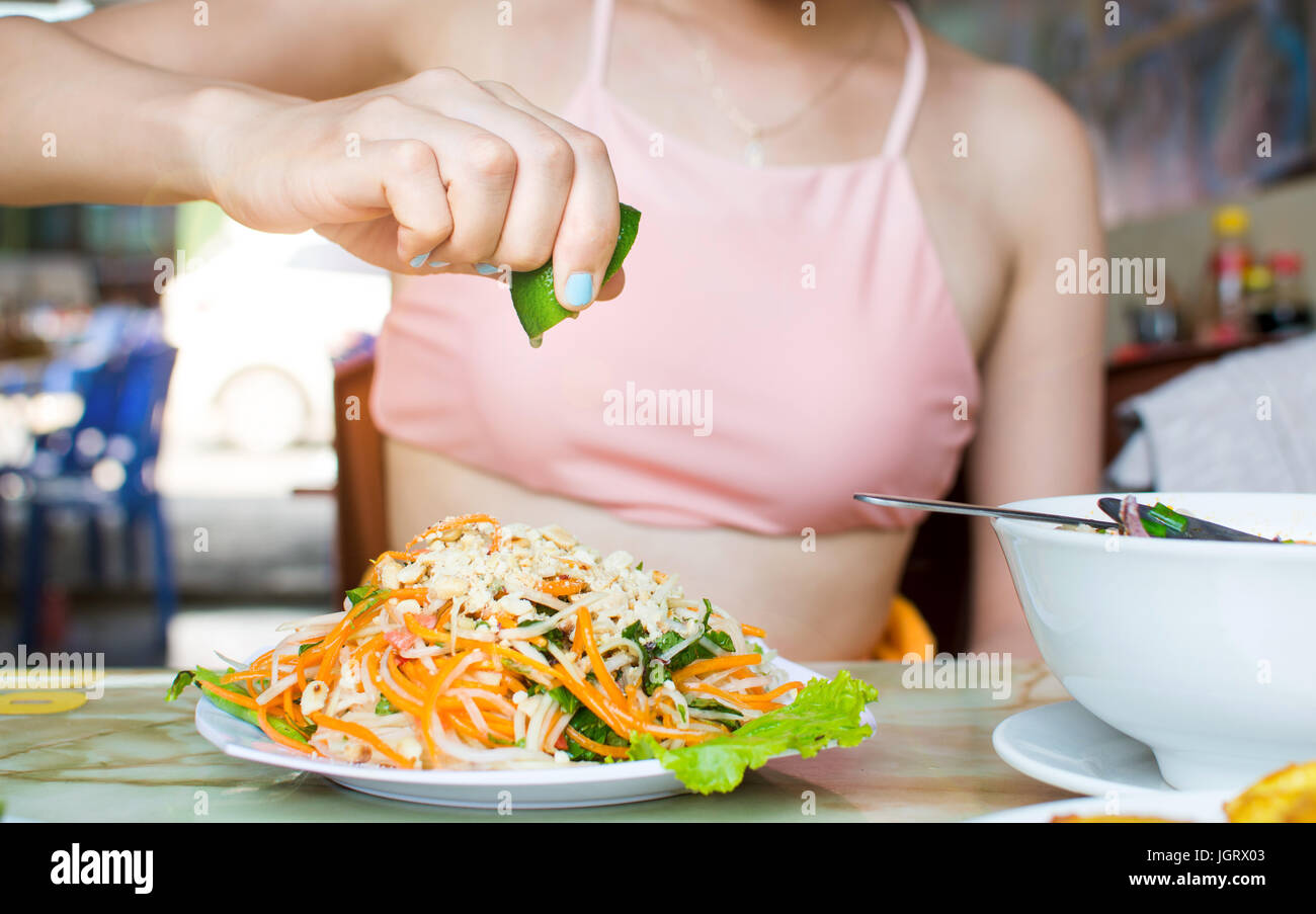 La main féminine squeezing lime sur Thai salade de papaye verte Banque D'Images