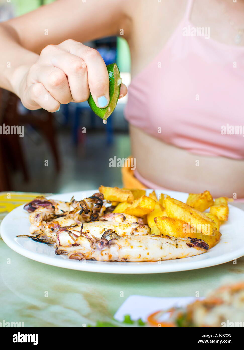 La main féminine squeezing lime sur Calmar grillé avec frites Banque D'Images