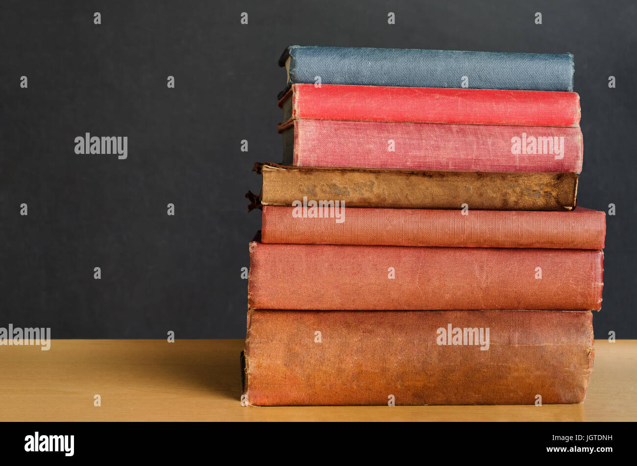 Près d'un coup de vieux, miteux, bien utilisé les livres empilés dans une pile sur un bureau devant un tableau noir. Copie de l'espace sur le côté gauche. Banque D'Images