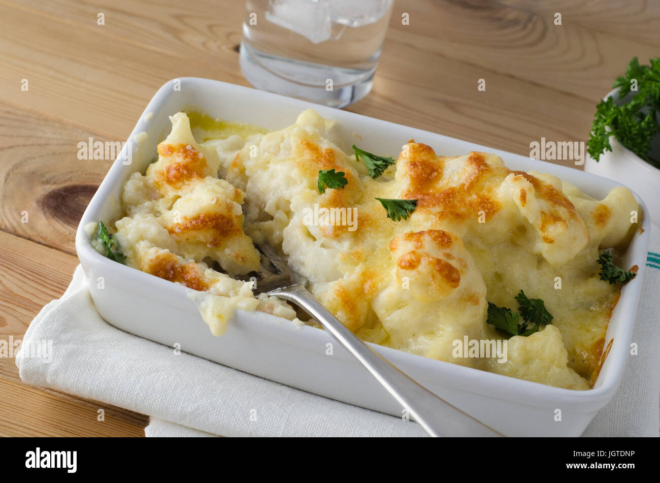 Repas sur une planche en bois de pin table. Un plat de chou-fleur cuit, fromage d'or parsemé de feuilles de persil frais. Fourche argent inséré comme si dini Banque D'Images