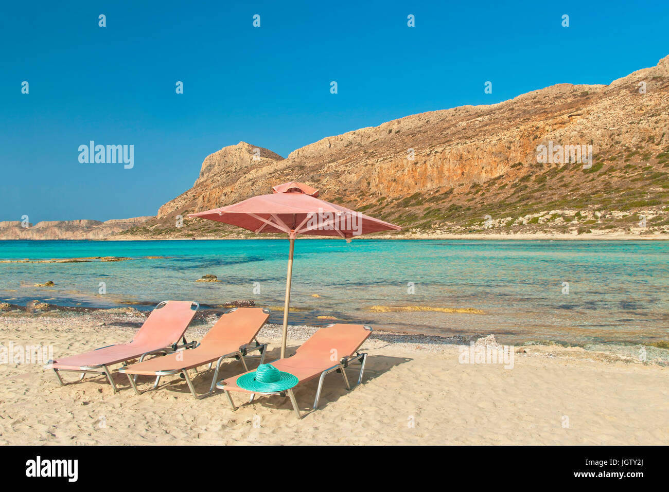 Trois chaises longues rose bleu avec chapeau et parapluie sur plage de Balos Bay sur l'île de Crète en Grèce, soleil du soir Banque D'Images