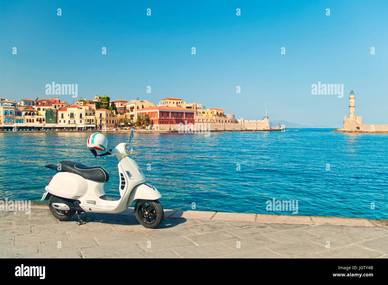 L'image traitée de style rétro blanc scooter stationné dans un port de Chania sur journée ensoleillée avec vieille ville vénitienne et phare à backgroun Banque D'Images