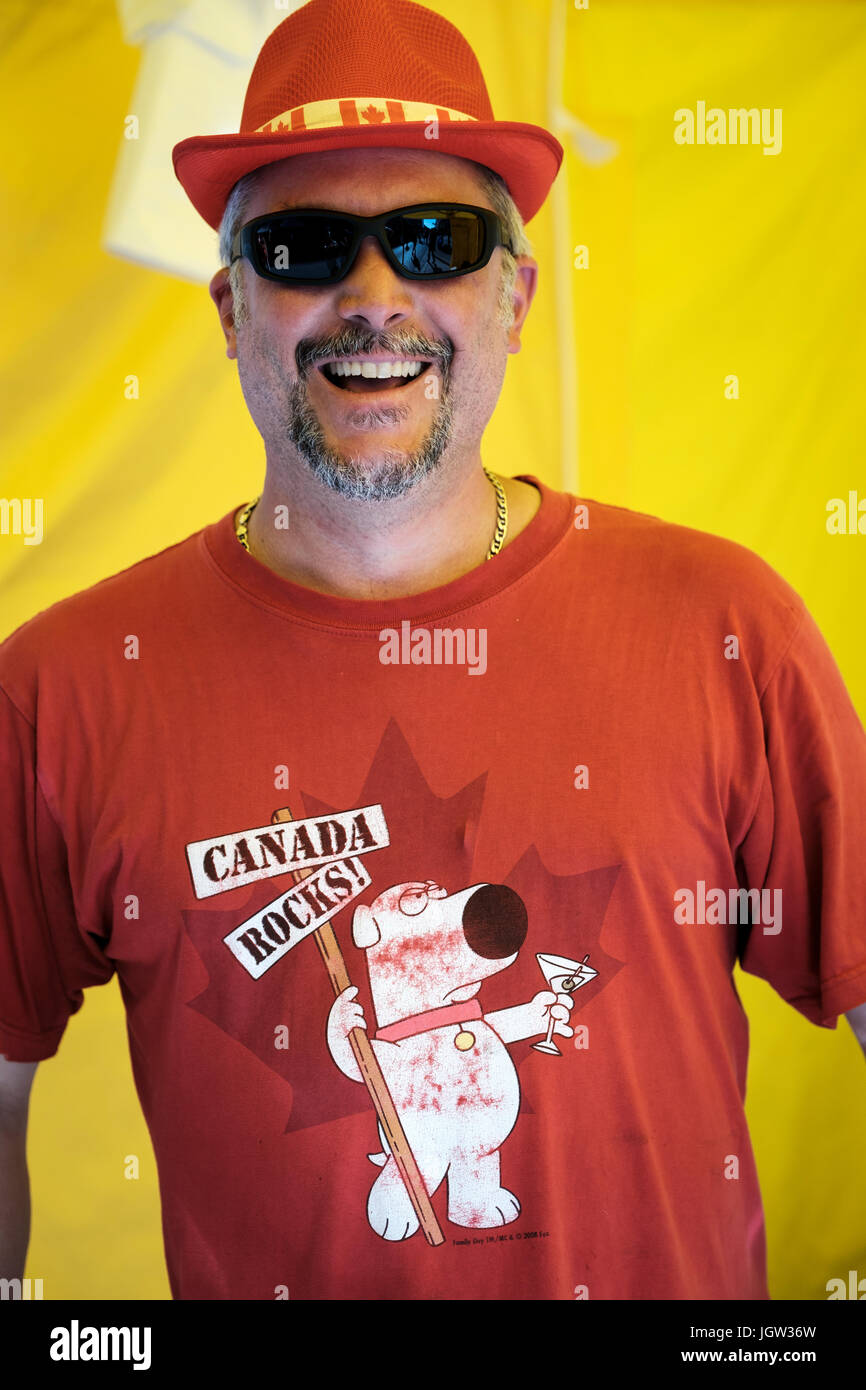 Homme d'âge moyen portant des lunettes de soleil, chapeau à thème canadien, t-shirt regardant la caméra, souriant à la caméra, pour célébrer le 150e anniversaire du Canada. Banque D'Images