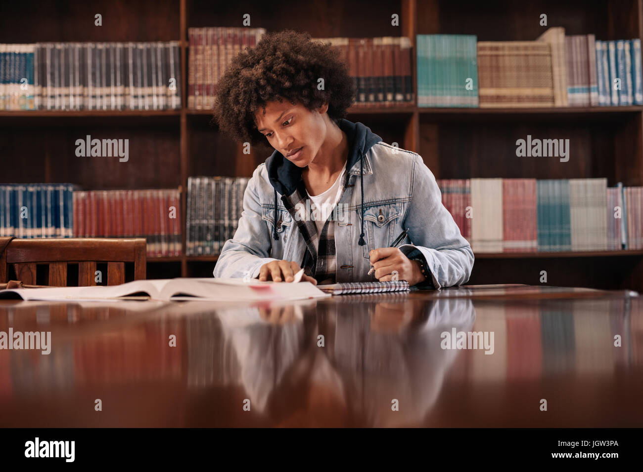 Les jeunes afro-américains l'homme assis à table avec des livres pour trouver de l'information en bibliothèque. Jeune étudiant de prendre des notes à partir de livres pour étudier en bibliothèque. Banque D'Images