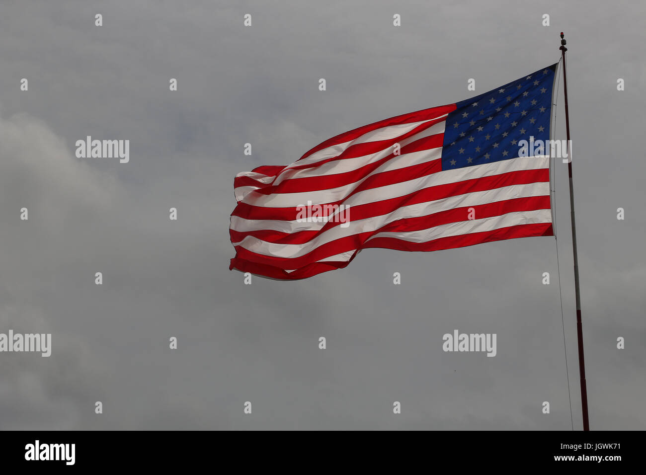 Le drapeau des États-Unis d'Amérique ou d'étoiles et de rayures au vent, contre un ciel couvert, gris, unfurled gauche, copier l'espace, sur un poteau. Banque D'Images