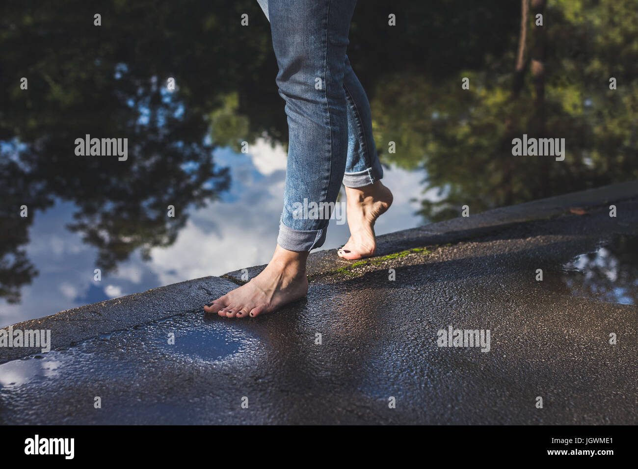 Nu-pieds femme en bleu jeans marche sur un bord de l'eau sur une chaussée  mouillée Photo Stock - Alamy