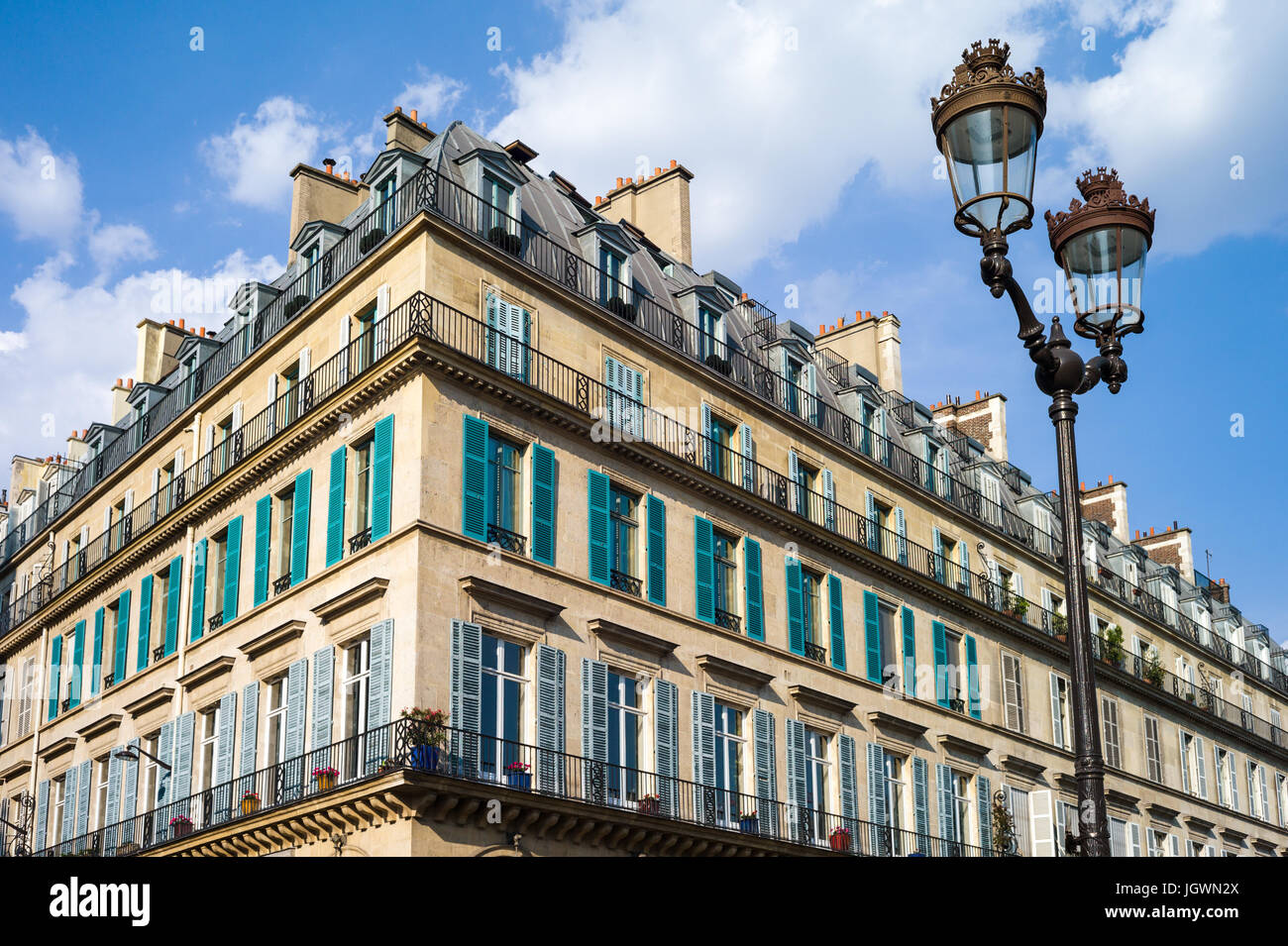 Un immeuble haussmannien typique à Paris avec balcon et volets et un lampadaire en premier plan sous une lumière chaude de fin d'après-midi. Banque D'Images