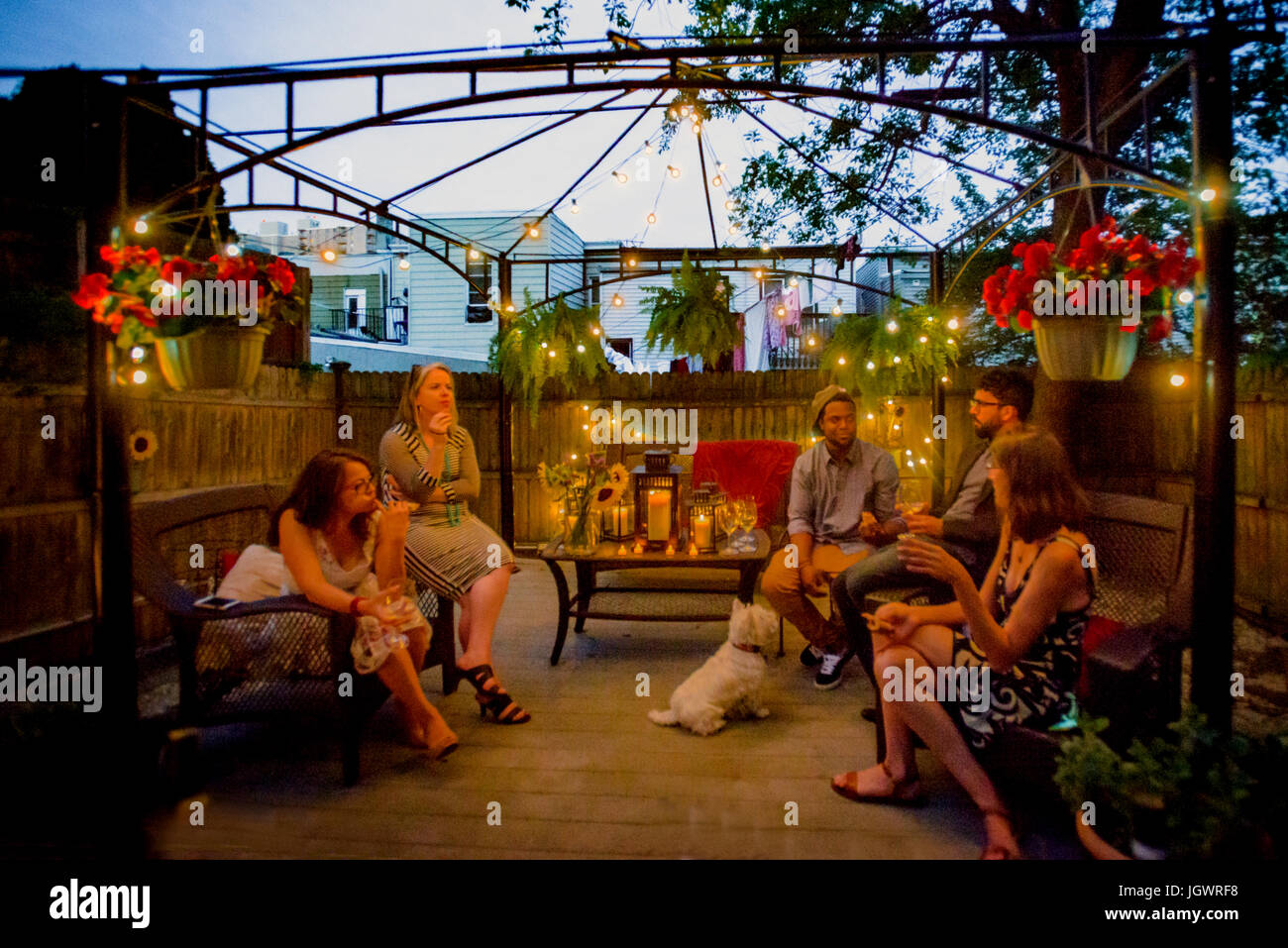 Groupe de personnes at garden party, assis sous pergola au crépuscule, boire du vin Banque D'Images