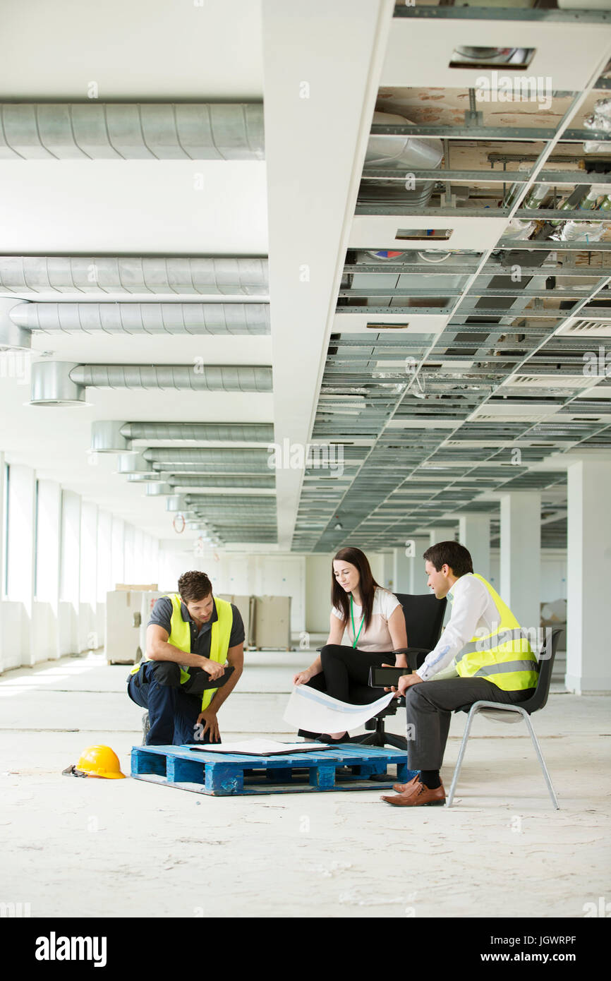 Trois personnes assises dans la construction de l'espace de bureau, regardant les plans de construction Banque D'Images