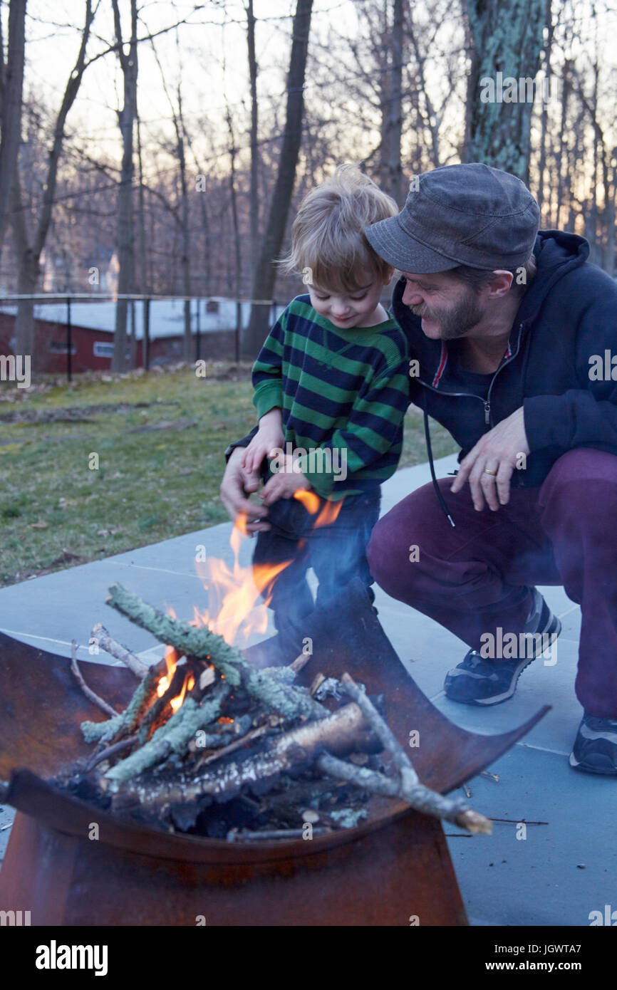 Garçon et père tendant le feu dans patio fire pit Banque D'Images