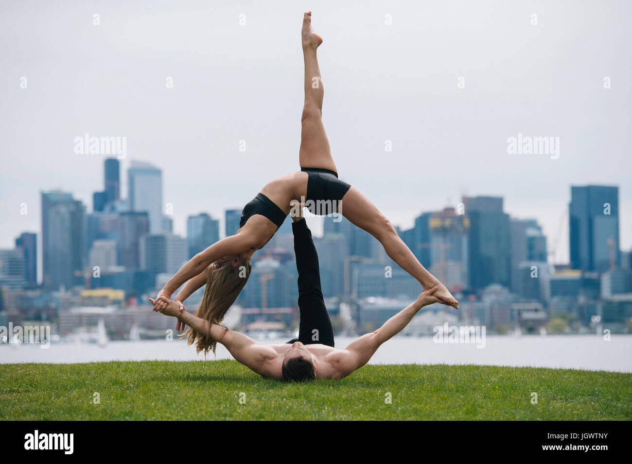 Jeune femme allongé sur le dos en équilibre sur les mains de l'homme, la pratique du yoga en face de Seattle skyline Banque D'Images