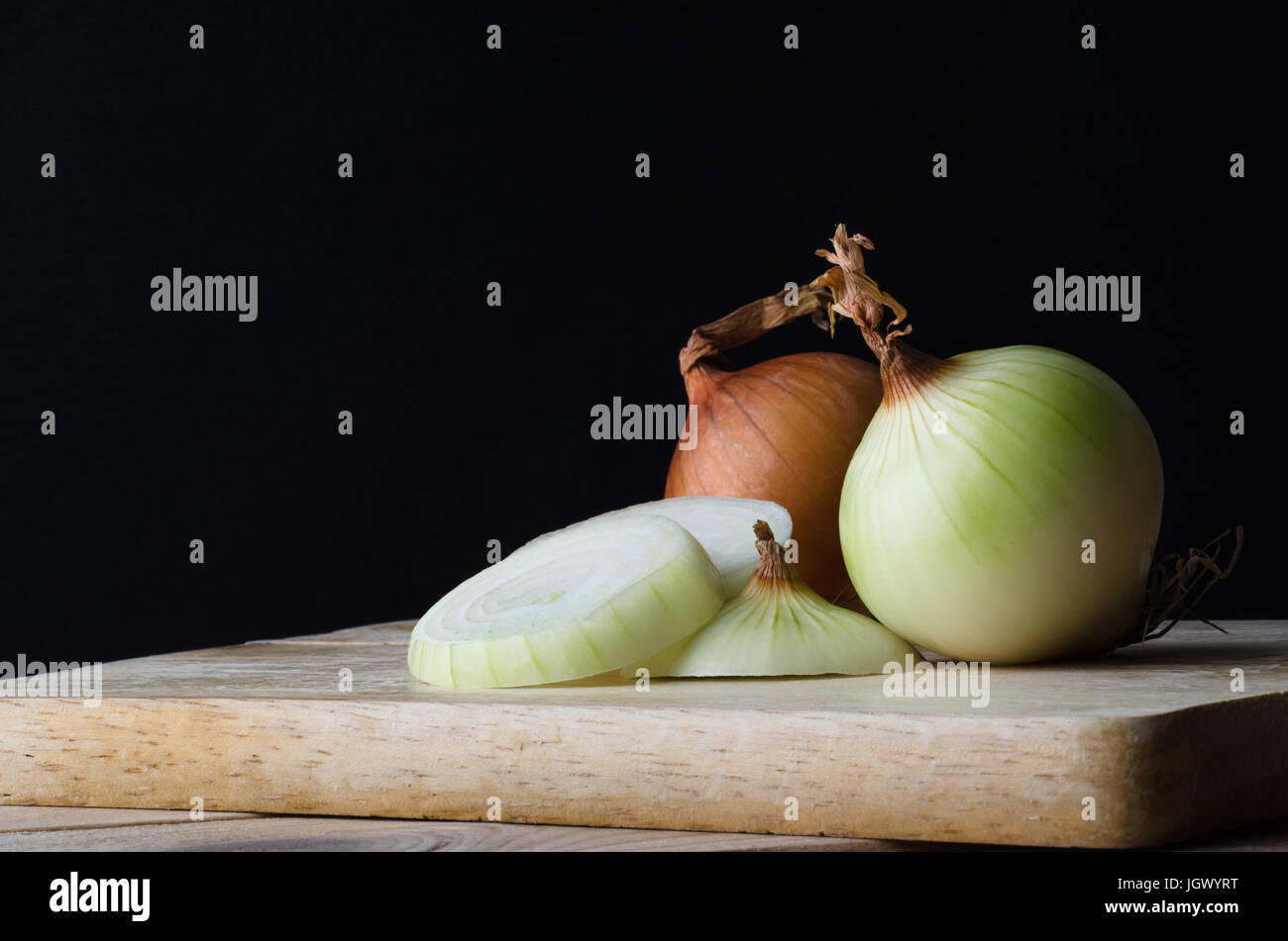 La vie encore la disposition des oignons, Entières, tranchées, pelées et non pelées sur une planche à découper de cuisine en bois sur un fond noir. Banque D'Images