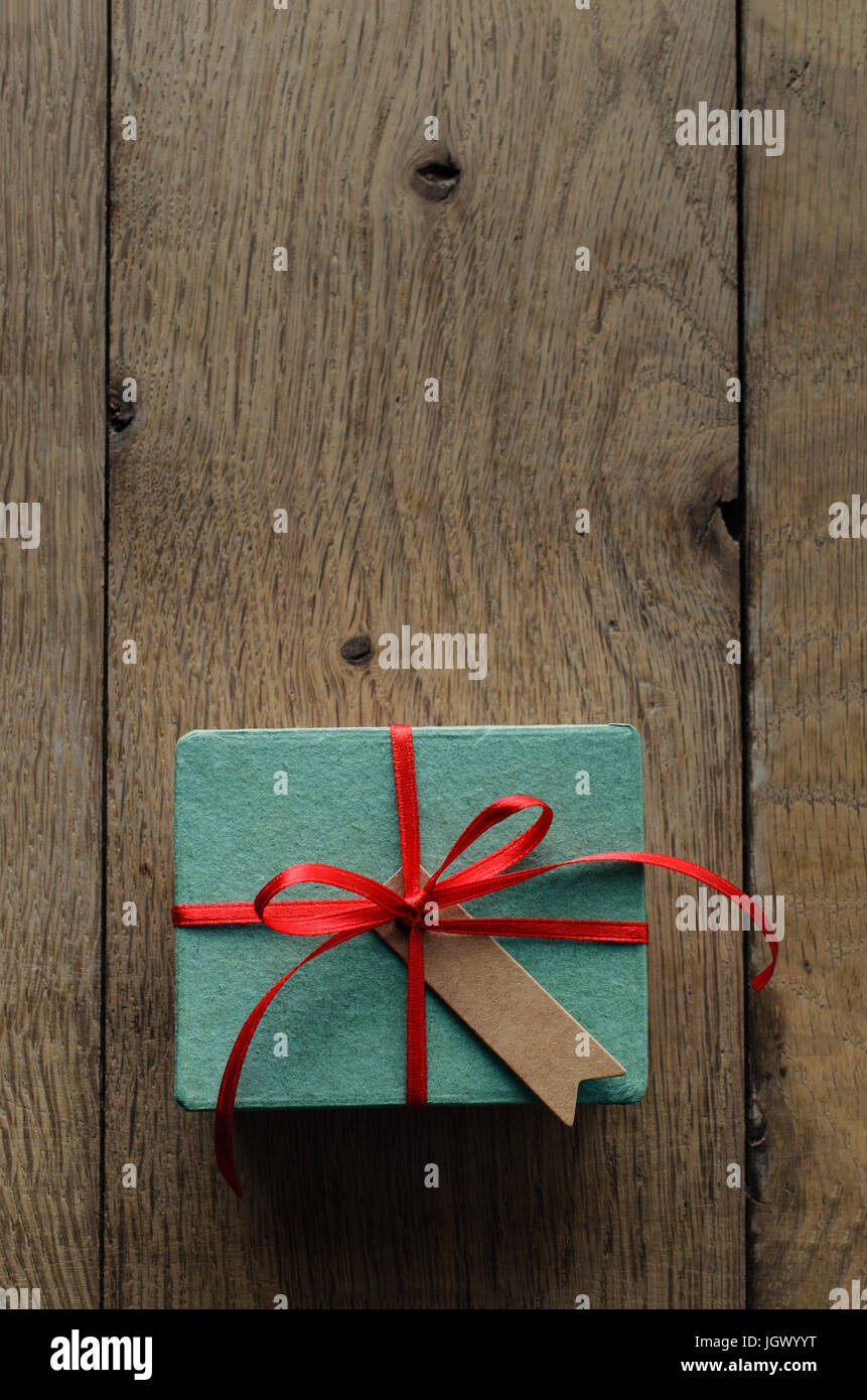 Passage tiré d'un coffret cadeau turquoise sur une table de planches de vieux bois de chêne, attaché à un noeud avec un ruban de satin rouge, avec un style vintage blanc tag message fa Banque D'Images