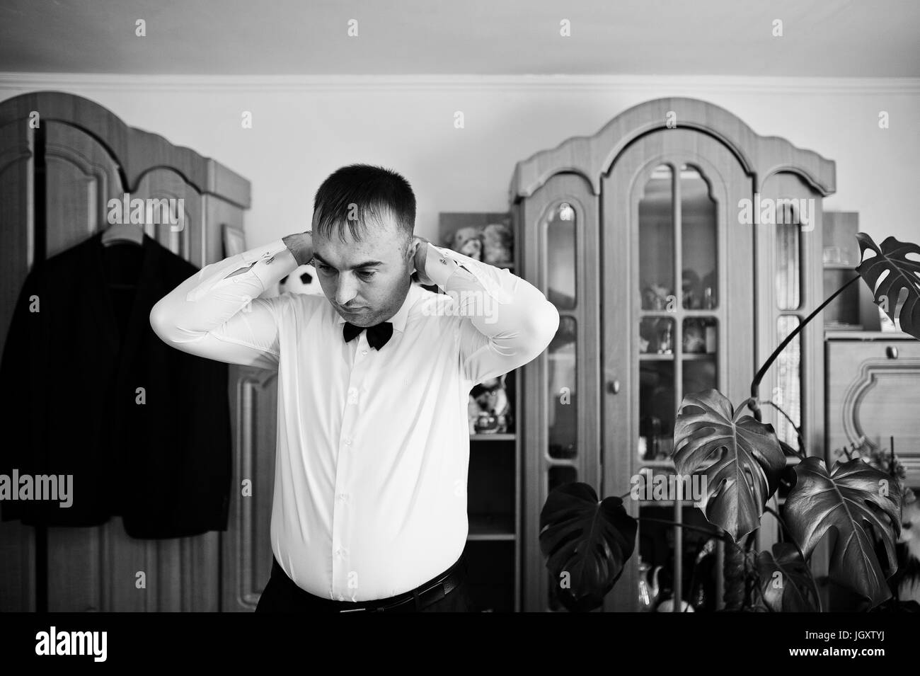 Beau palefrenier s'habillant dans sa chambre pour sa cérémonie de mariage. Photo en noir et blanc. Banque D'Images