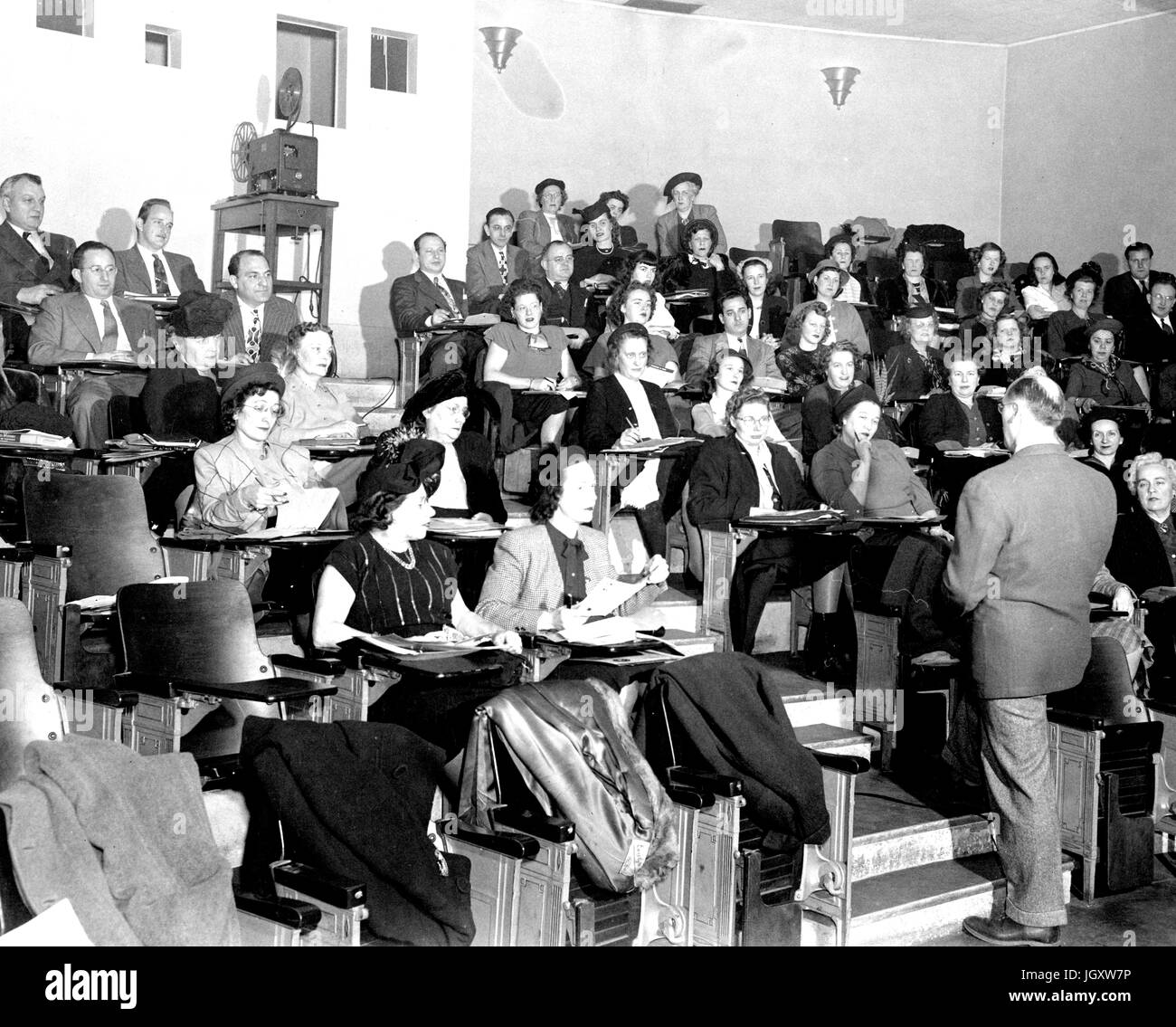 Les étudiants du collège soirée JHU s'asseoir dans une salle de conférences en prenant des notes que leur professeur se trouve dans les couloirs des conférences, 1930. Banque D'Images