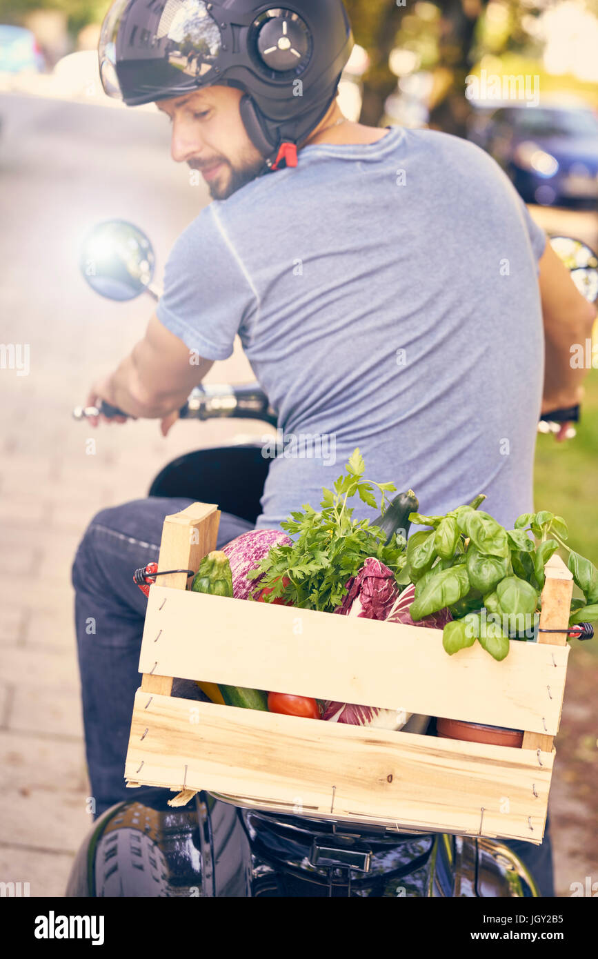 Vue arrière de l'homme sur la moto transportant des légumes dans la caisse Banque D'Images