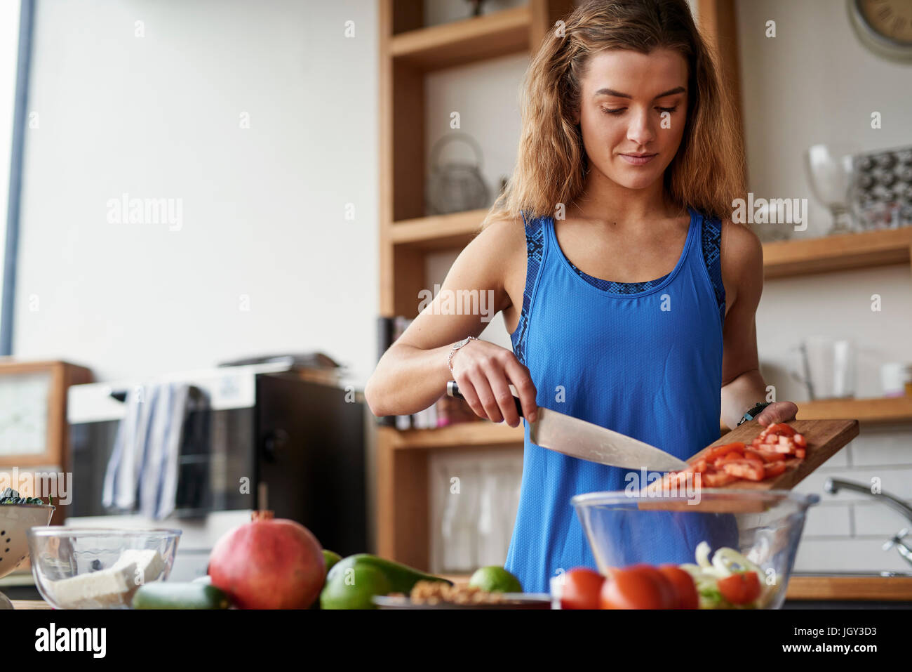 Jeune femme à la table de cuisine slicing tomatoes Banque D'Images