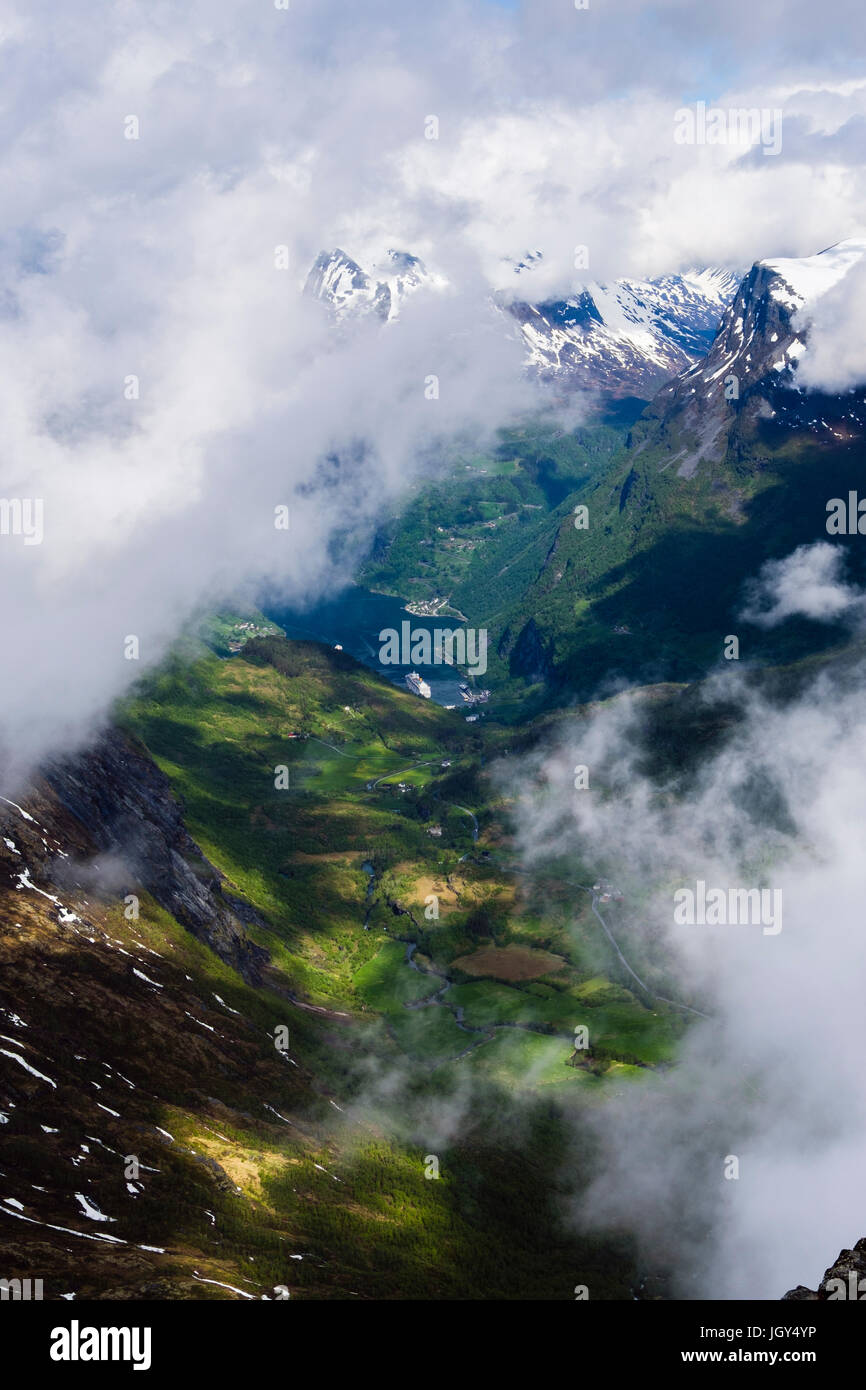 Vue vers le bas à travers les nuages de Geirangerfjorden avec montagnes aux sommets enneigés de la montagne Dalsnibba en été. Sunnmøre, Geiranger, Norvège Møre og Romsdal Banque D'Images