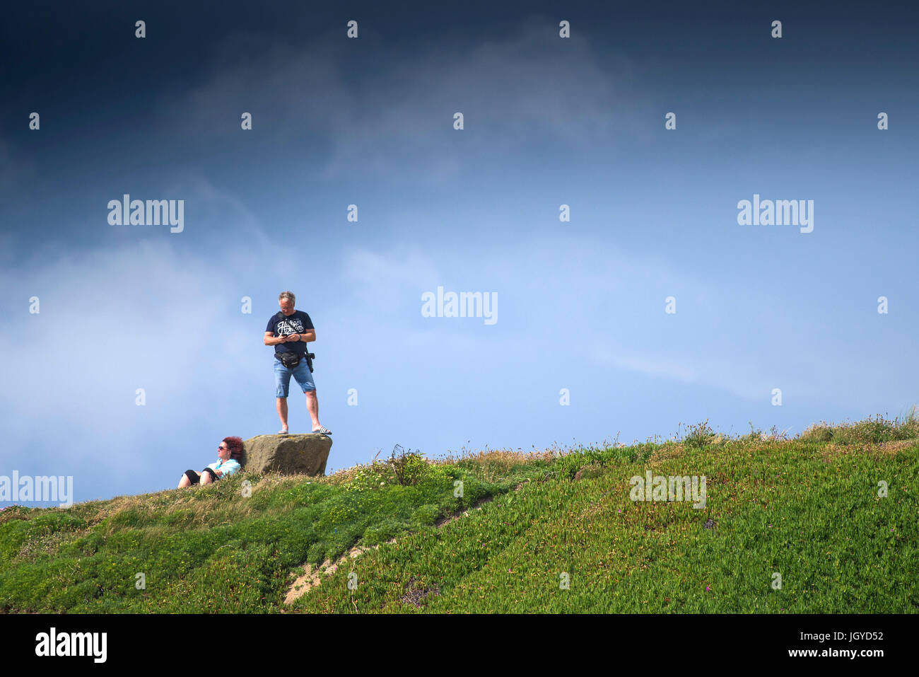 Un homme debout sur un rocher et une femme se détendre au soleil sur la plage à Newquay, Cornwall. Banque D'Images