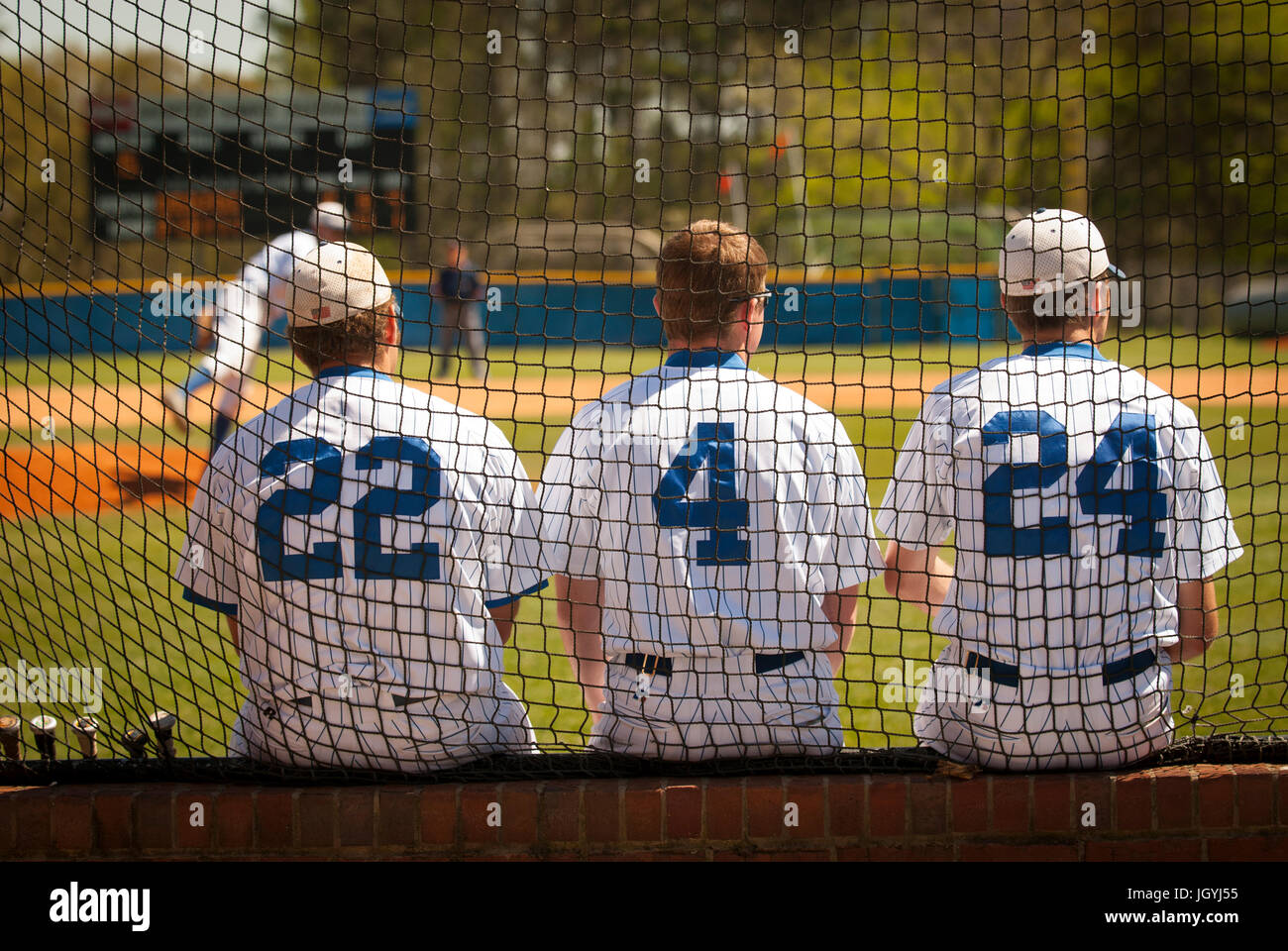 Trois joueurs de base-ball sur le banc dans un collège d'un match de baseball en regardant le lanceur. Banque D'Images