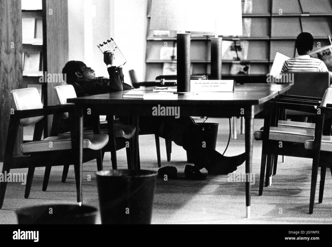 Un étudiant de l'Université Johns Hopkins se penche en arrière dans sa chaise de lire un livre à une table dans l'Université s'Milton Eisenhower Library, à Baltimore, Maryland, 1965. Banque D'Images
