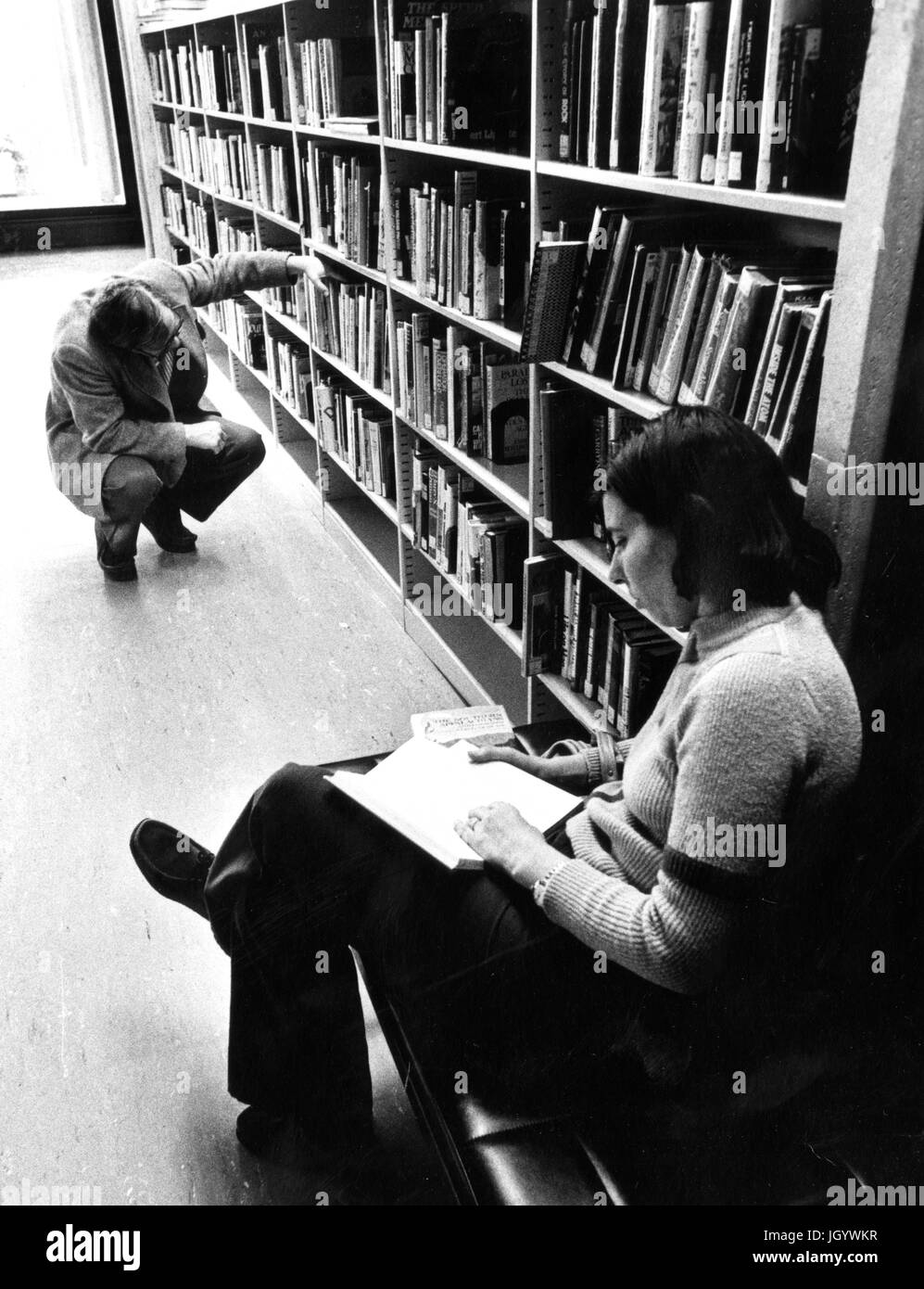 Candid portrait de deux étudiants de l'Université Johns Hopkins, assis dans les piles de lecture et à la recherche de livres à l'université, Milton S Eisenhower Library, à Baltimore, Maryland, 1965. Banque D'Images