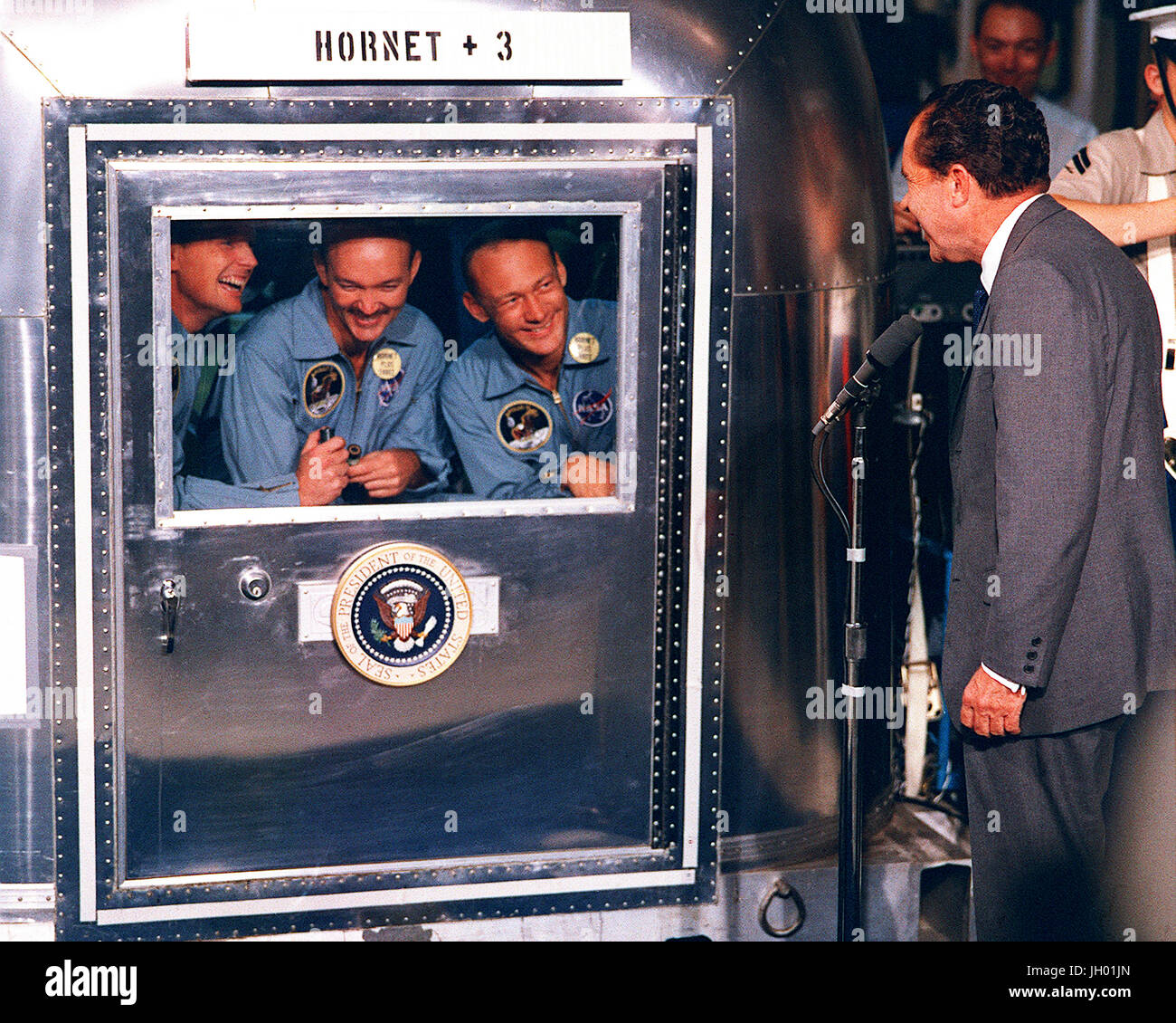 Le président Richard M. Nixon se félicite de l'Apollo 11 astronautes à bord du U.S.S. Hornet, le navire de récupération de l'historique mission Apollo 11 lunar landing. Limitée à l'installation de quarantaine Mobile (MQF) sont Neil A. Armstrong, commandant ; Michael Collins, pilote du module de commande ; et Edwin E. Aldrin Jr., pilote du module lunaire. Banque D'Images