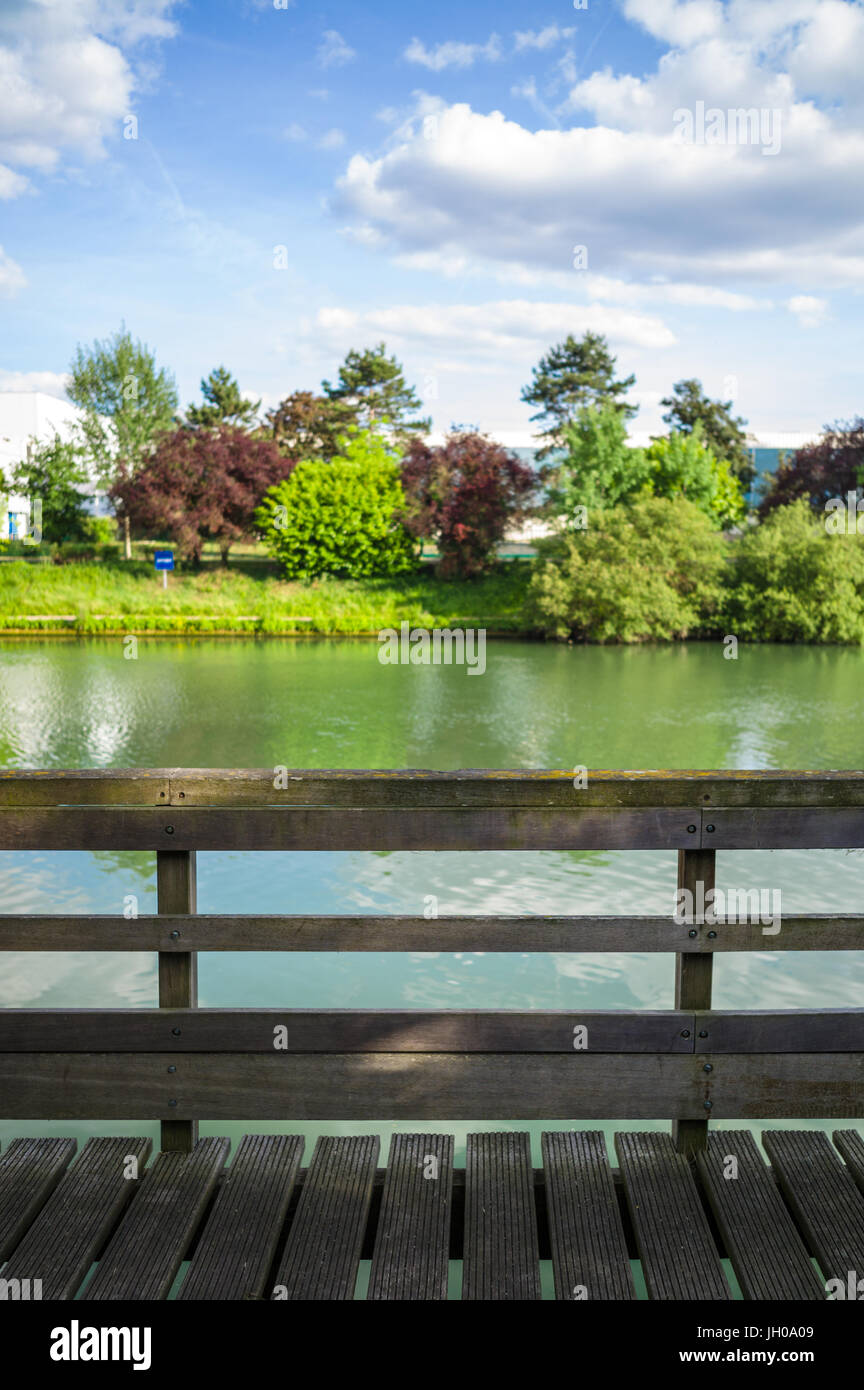 Un ponton en bois avec rampes en bois en face d'une rivière avec des arbres et de la végétation sous un ciel bleu avec des nuages blancs. Banque D'Images